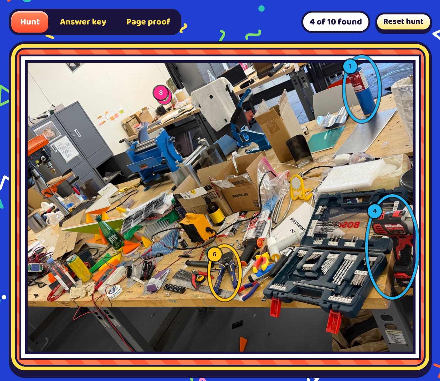 Hunt mode on the studio workbench photo with 4 of 10 found: the blue gas tank, the red drill, the blue pliers and the orange dog are circled, and the rest stay hidden.